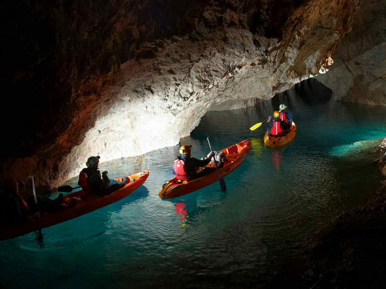 Kayaks in a dark cave lit by torches in Peca, Slovenia