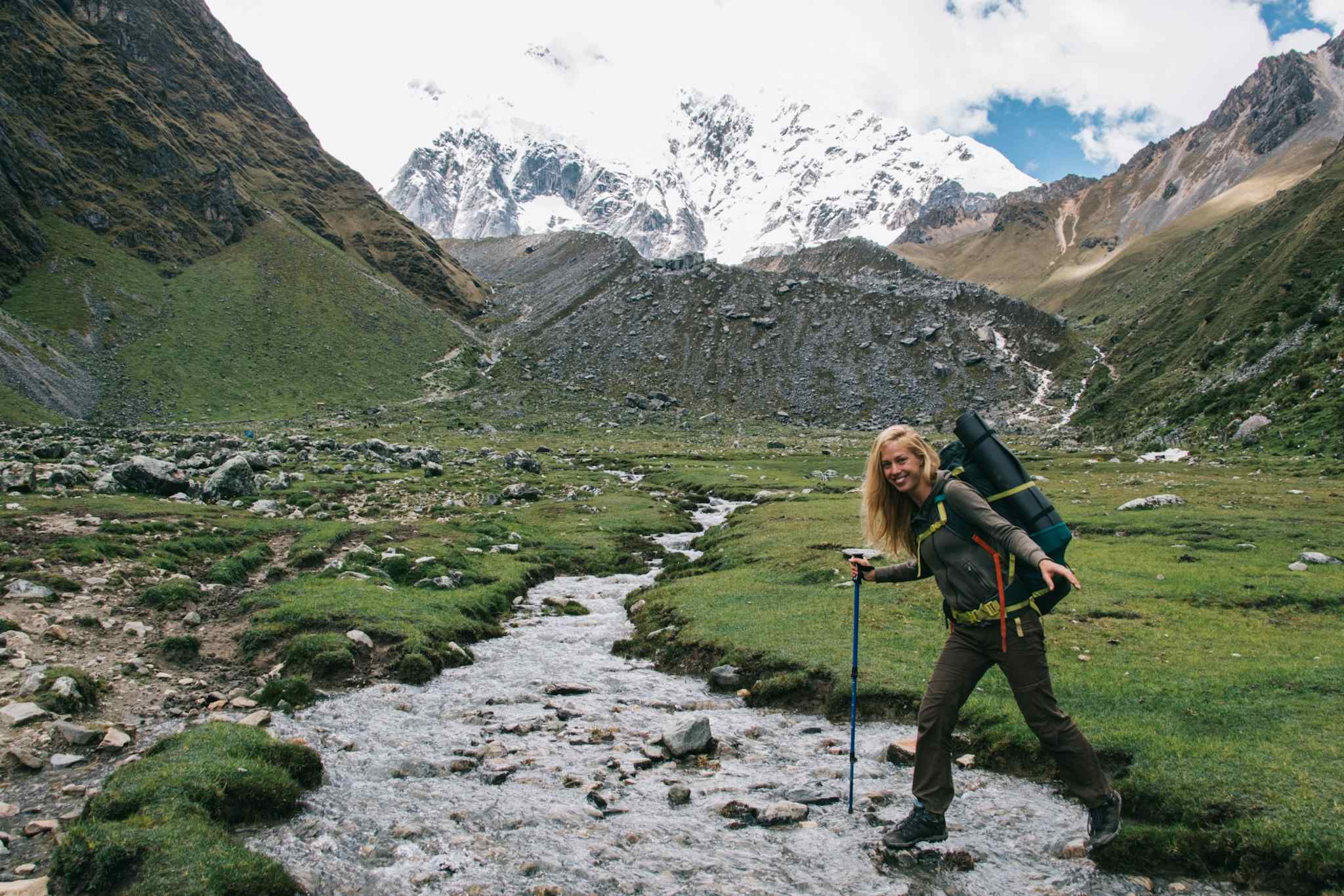 Women crossing a river on the Salkantay Trek in Peru with snow-covered mountains in the background