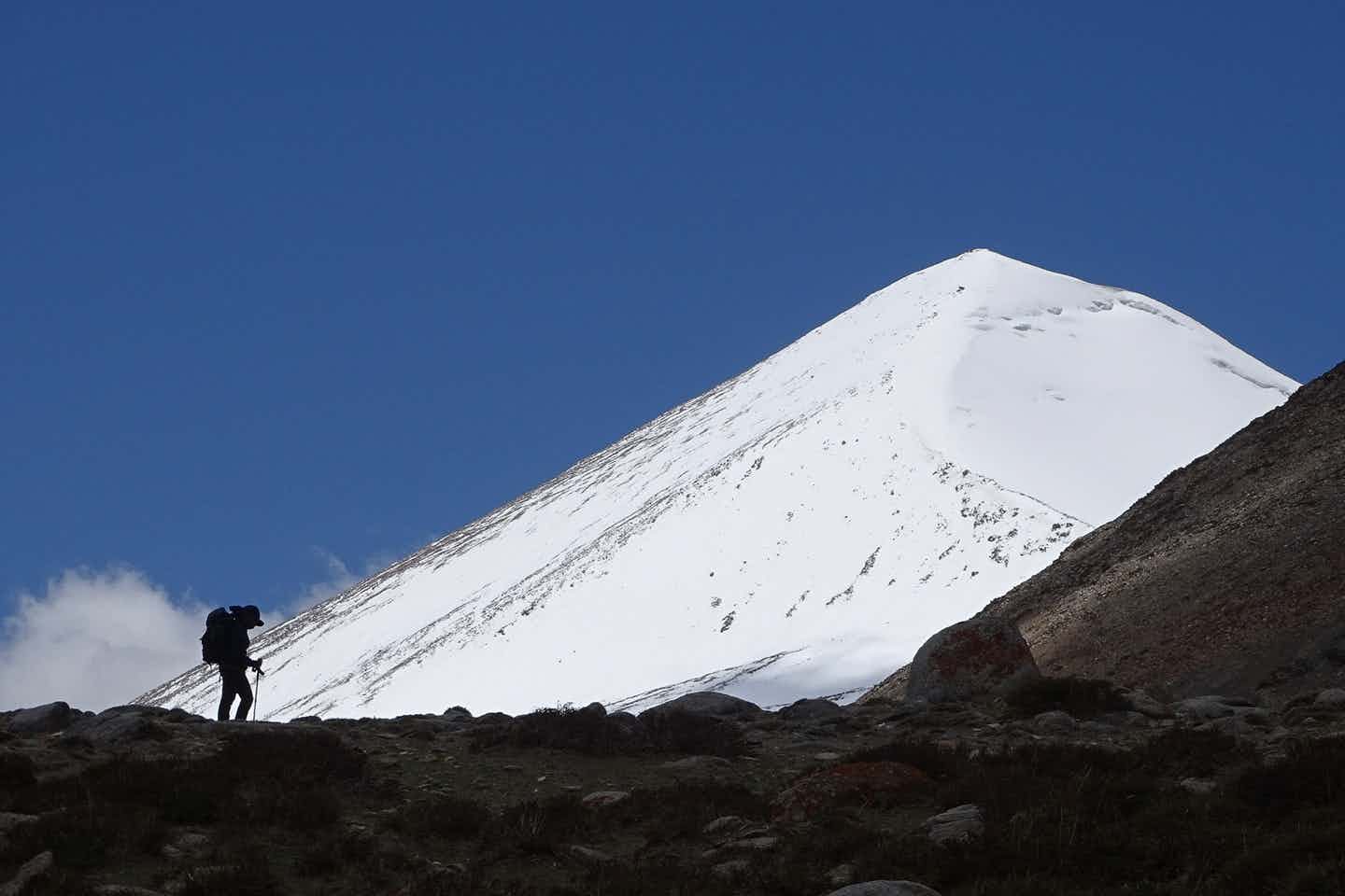 Lone hiker silhouetted against the snowy peak of UT Kangri from base camp in Ladakh, India