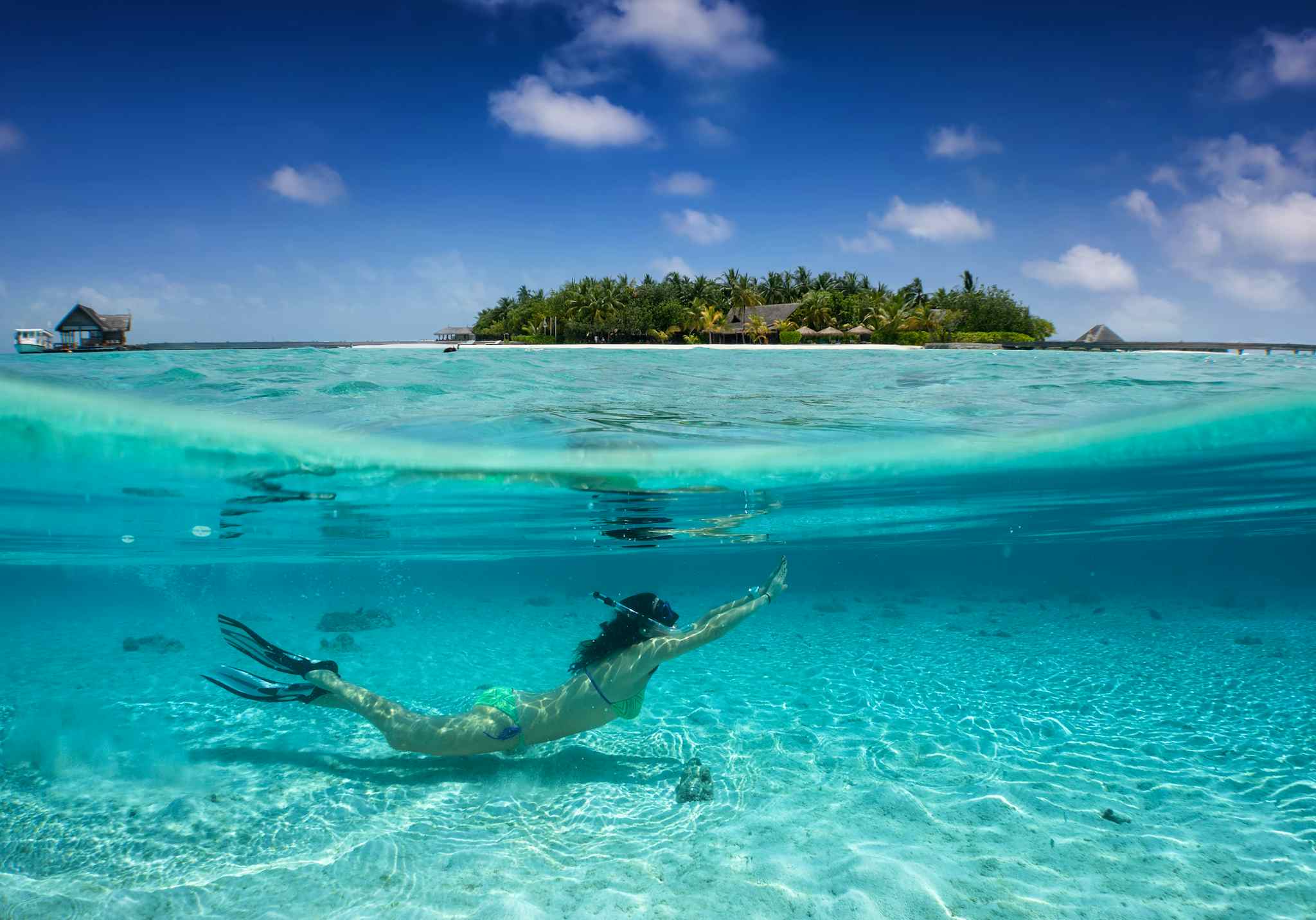 Woman snorkelling in the Maldives with island in the background.