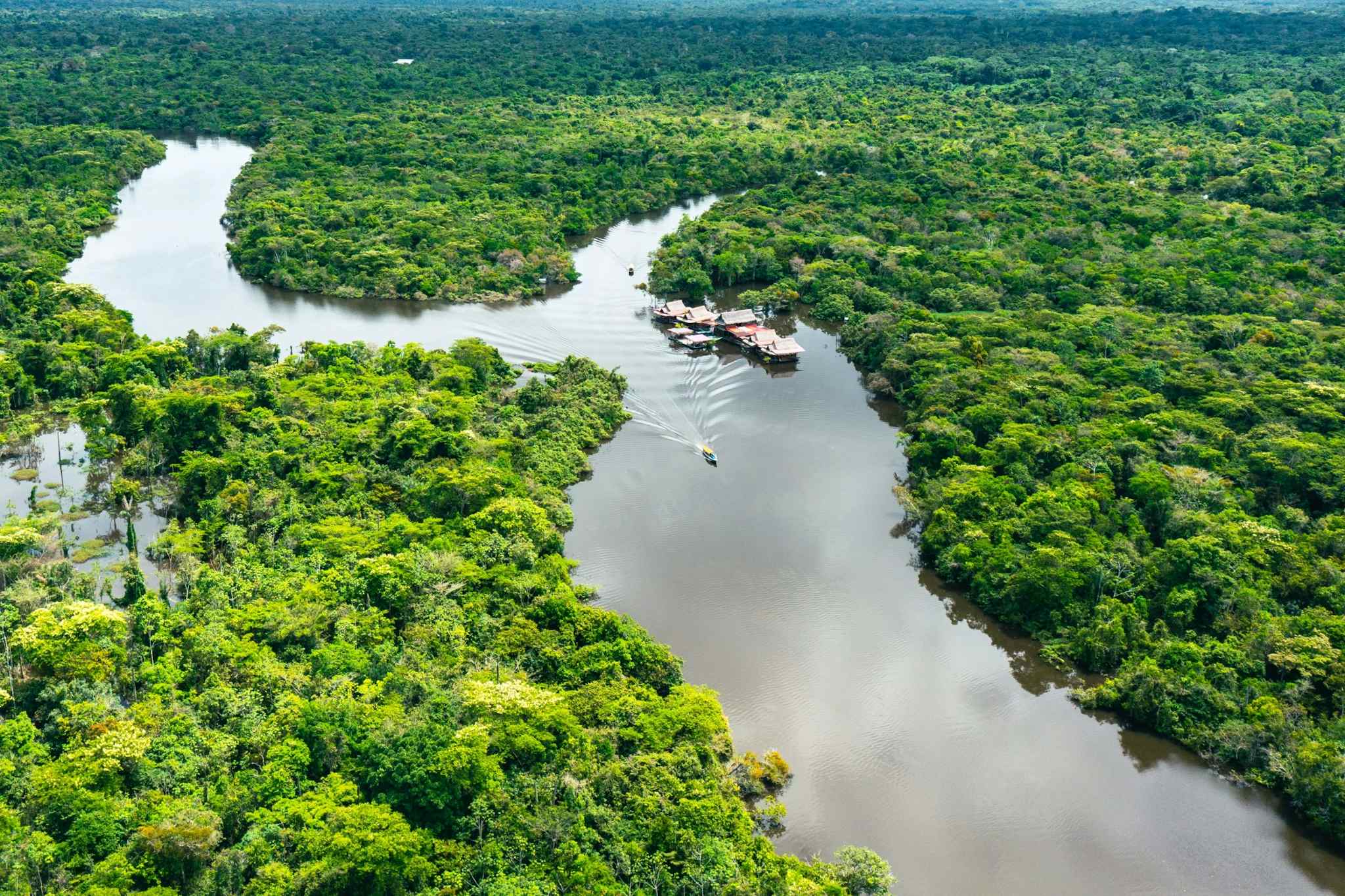 Boat travelling past a riverside village in the Amazon Rainforest in Peru