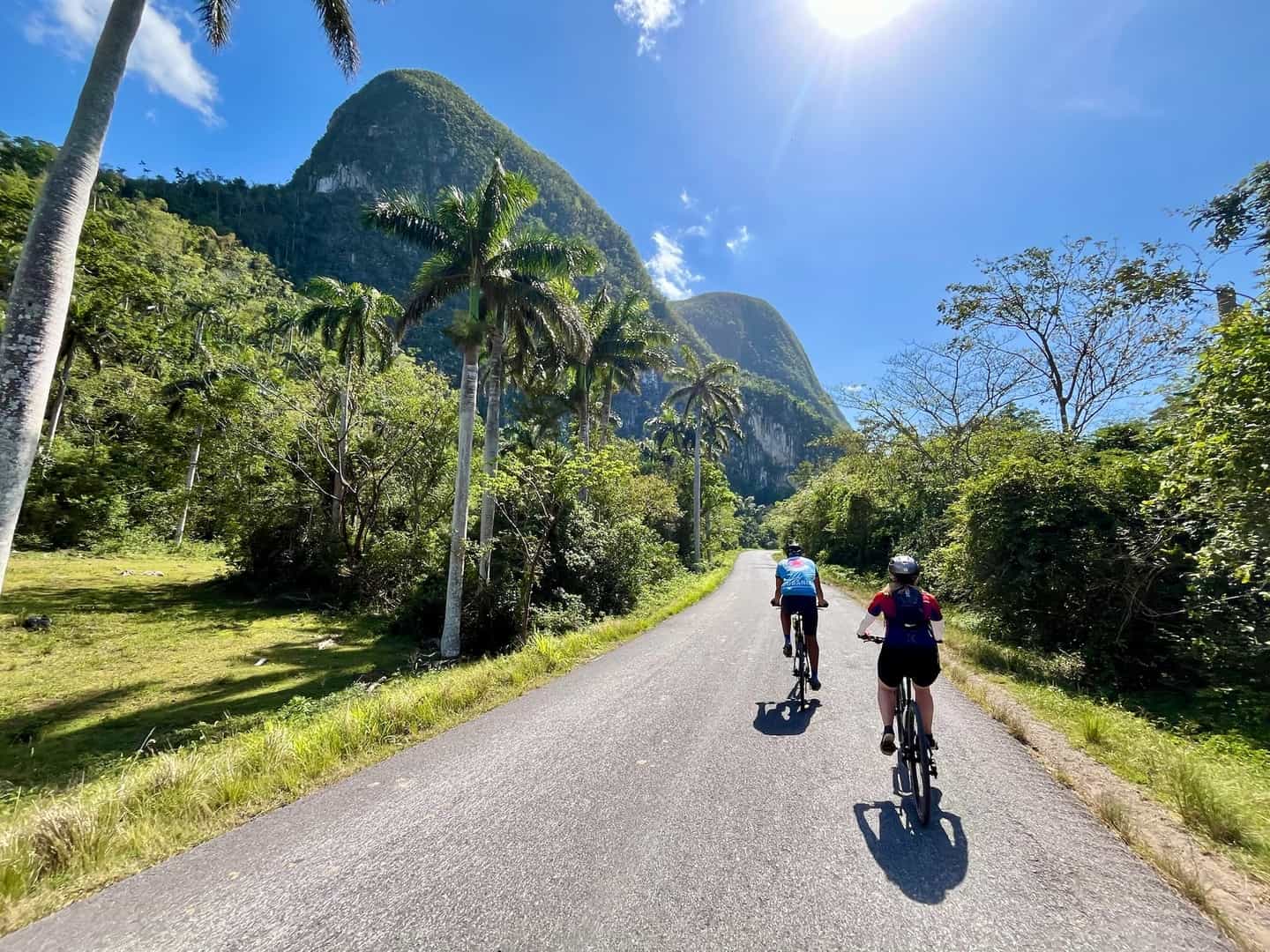 Two cyclists riding past mogotes and palm trees in Cuba