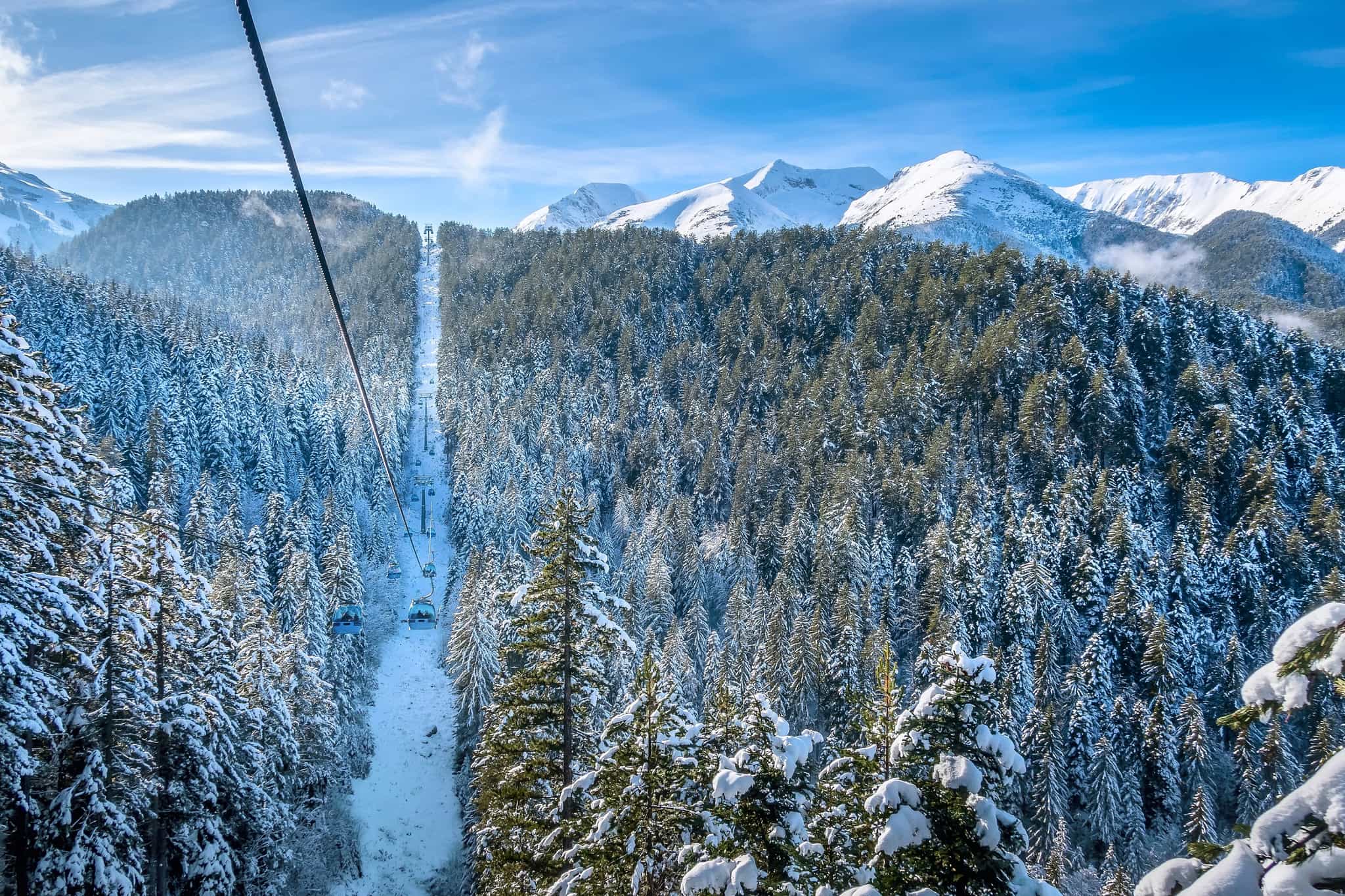 Chairlift through the forest with high snow covered mountains in the background