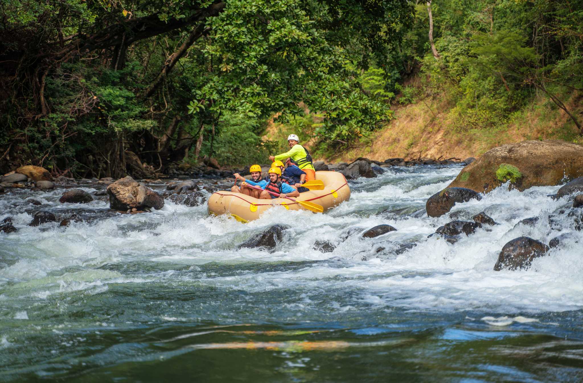 People on a yellow rafting floating down a river with white water in Costa Rica