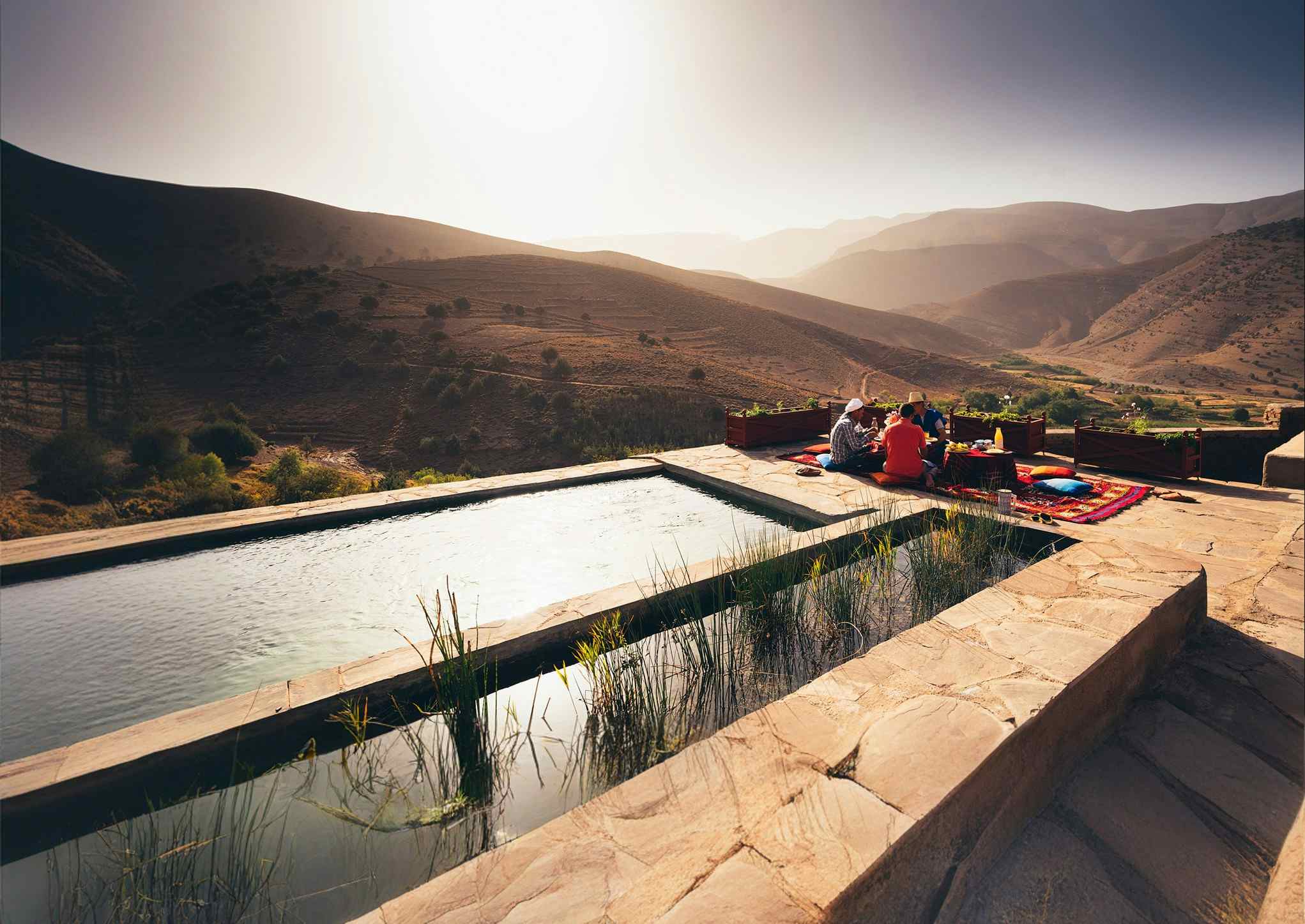 View of a pool and people eating food in front of the mountain view in Morocco.