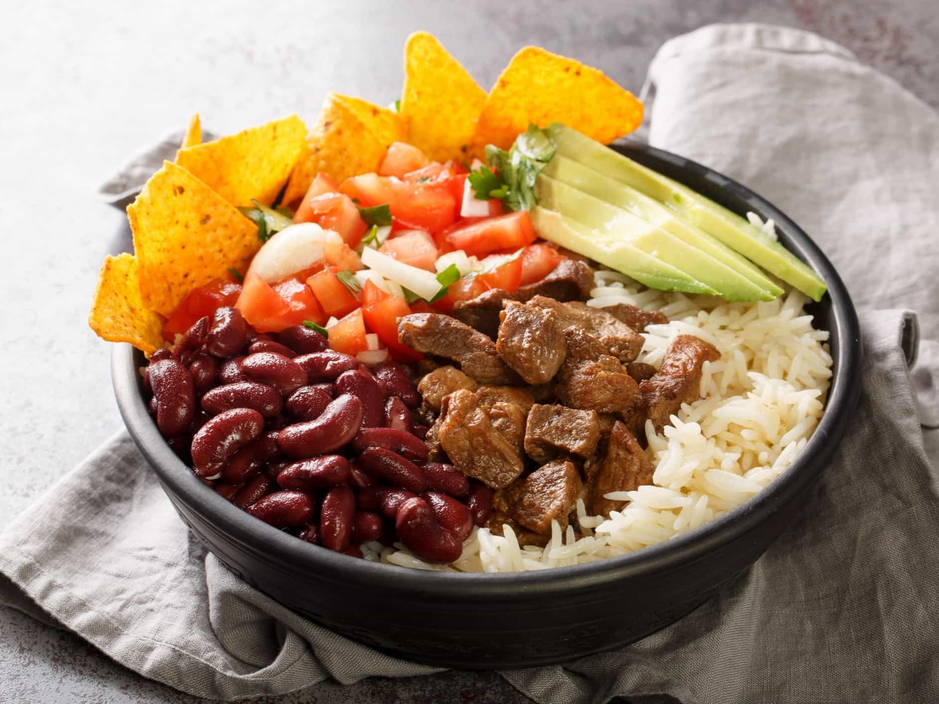 Costa Rican chifrijo is a layered dish of tender beans topped with chicharron and chimichurri served with tortilla chips closeup on the plate