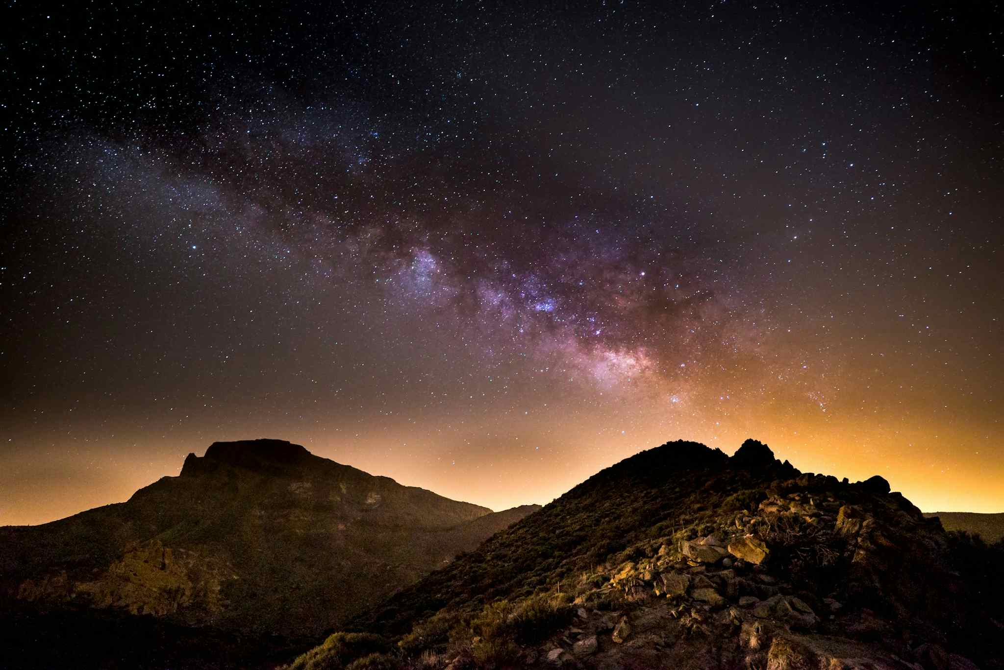 Starry sky at night with orange and purple light and the volcanic landscape of Tenerife below