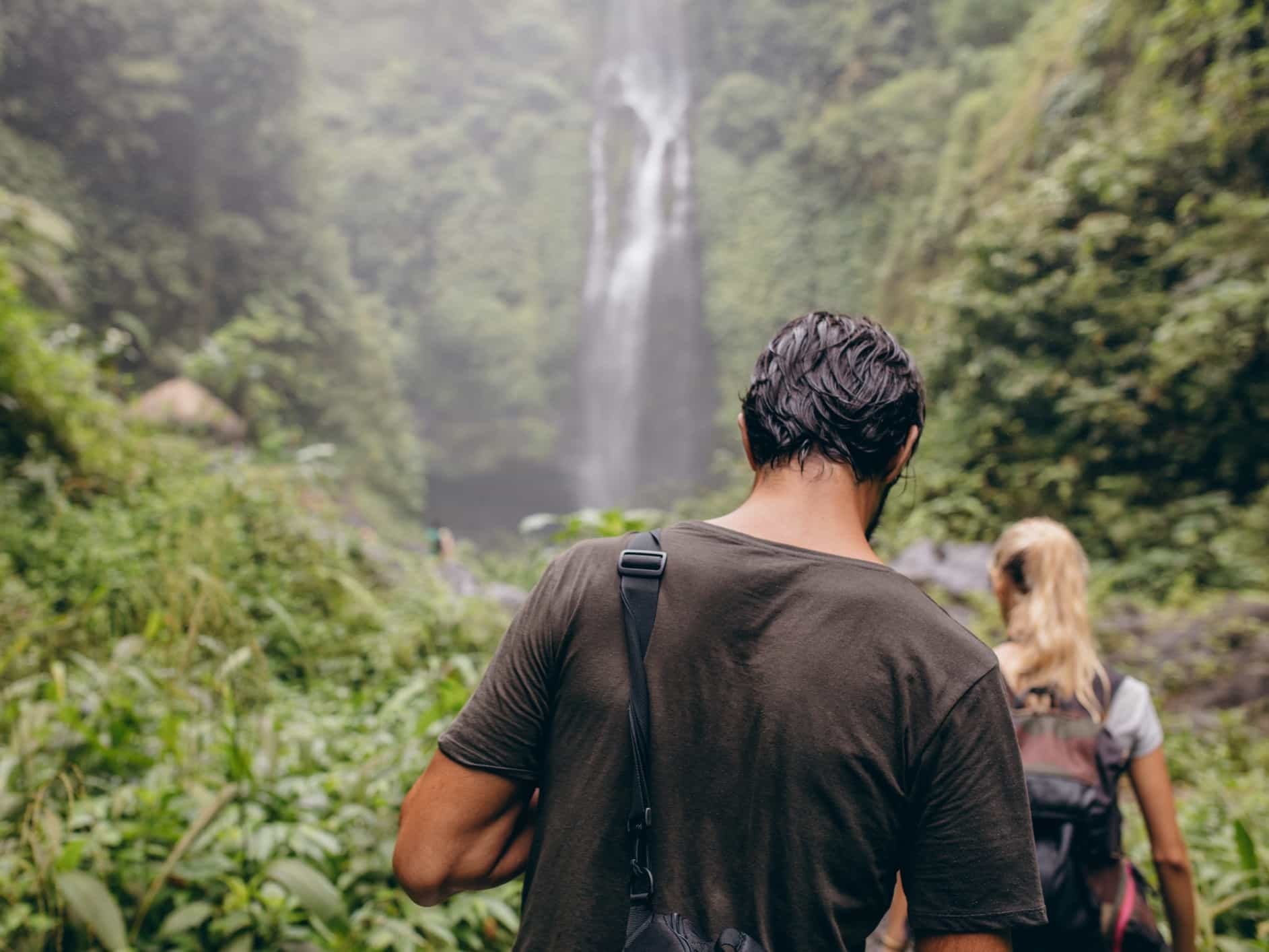 Rear view of young man and woman walking towards a water fall in forest.