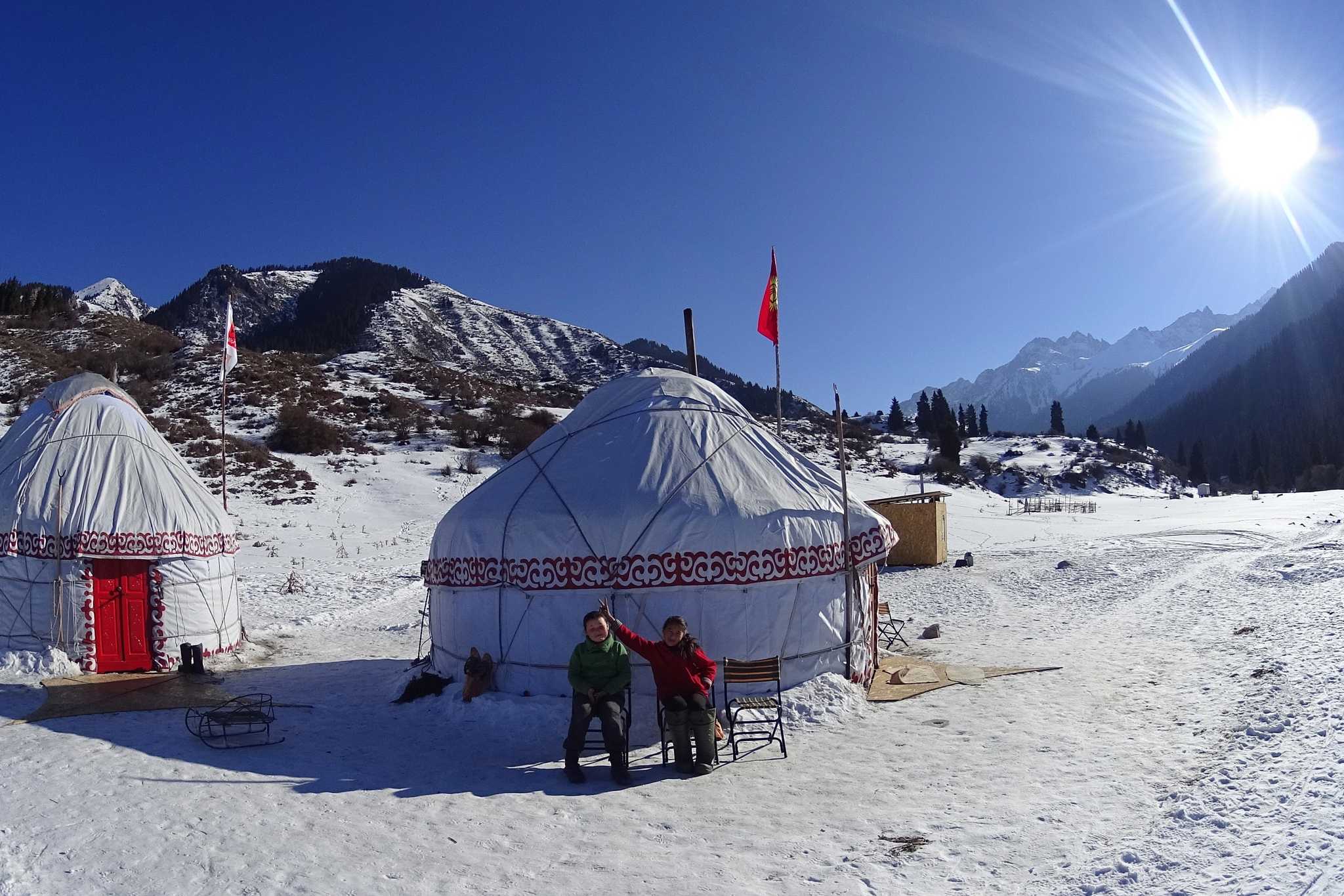 Two yurts in the snow with mountains behind in Kyrgyzstan