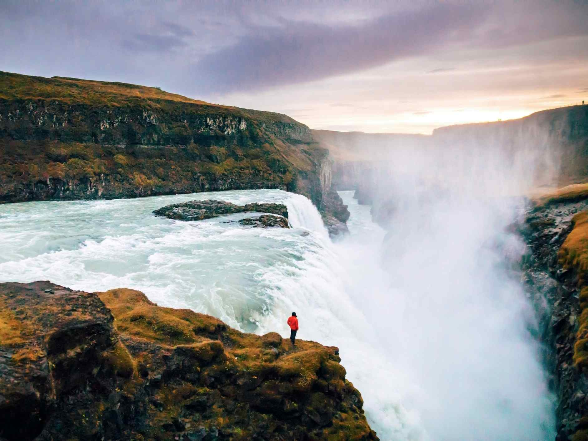 Person standing at the dramatic Gullfoss waterfall in Iceland.