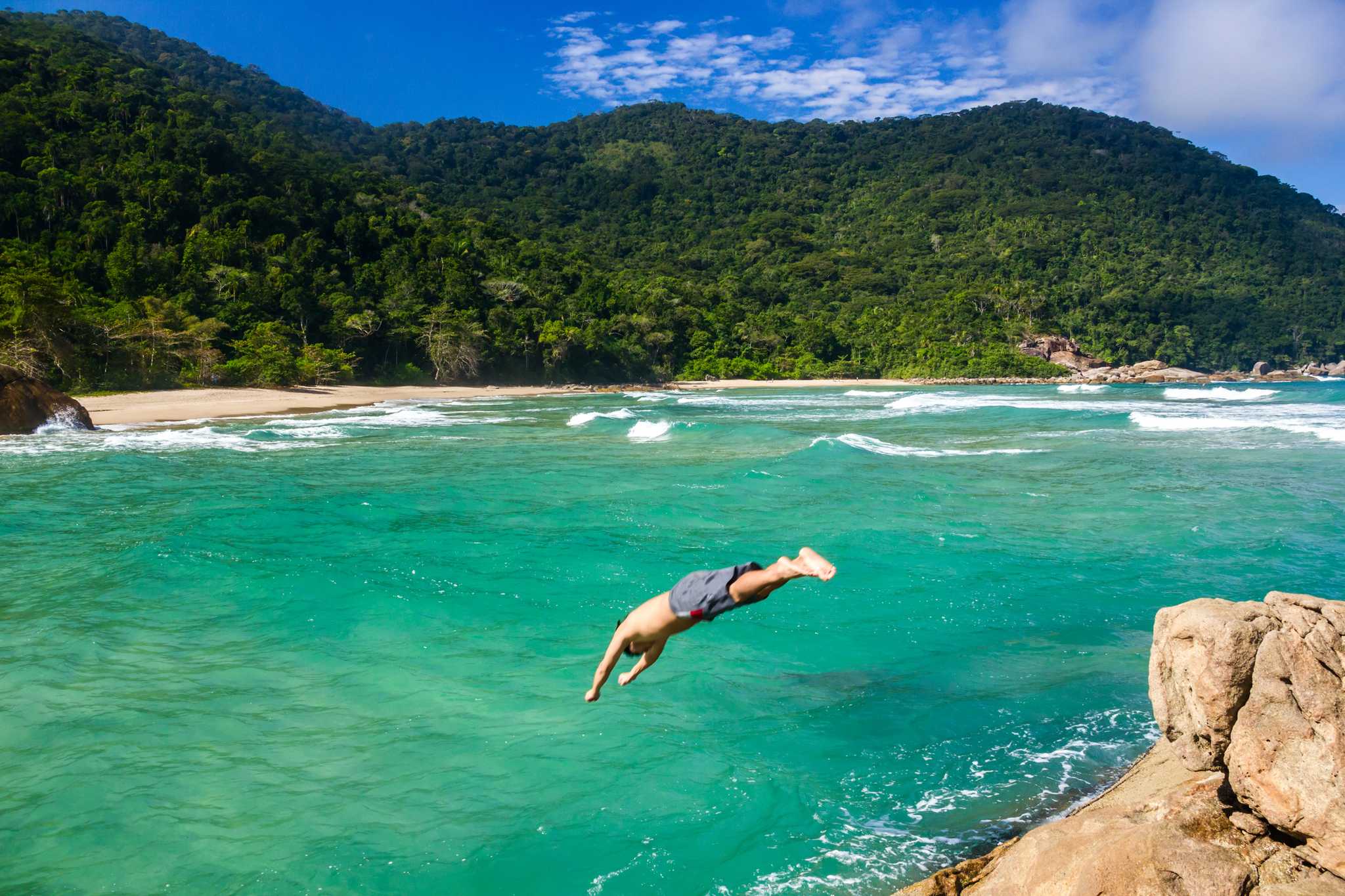 A man diving into the turquoise waters backed by forest in Paraty, Brazil.