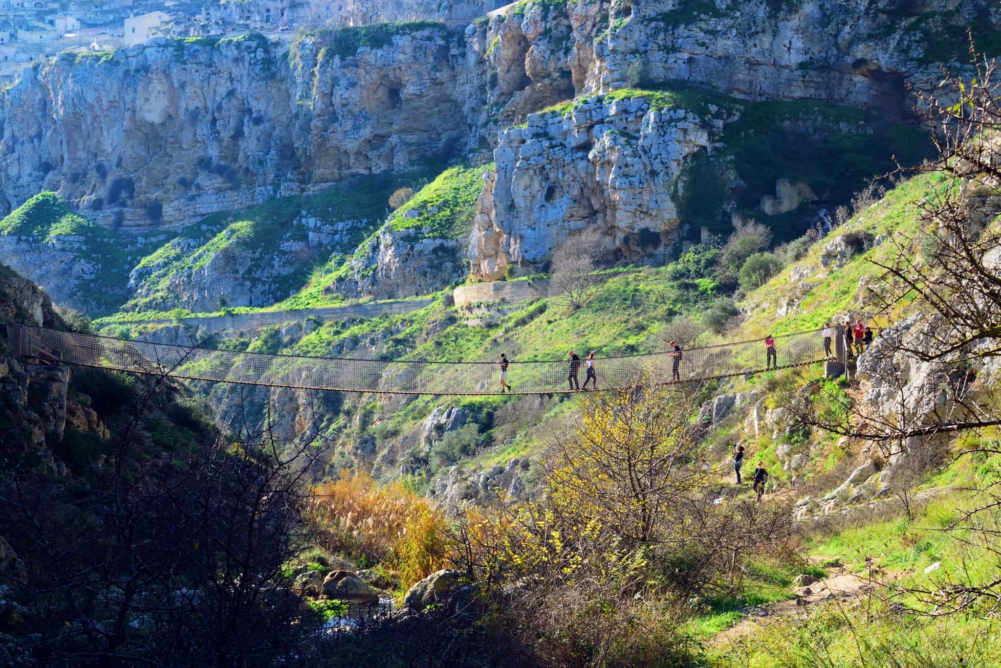 Hikers on a Tibetan-style suspension bridge in the Matera Canyon, Italy.