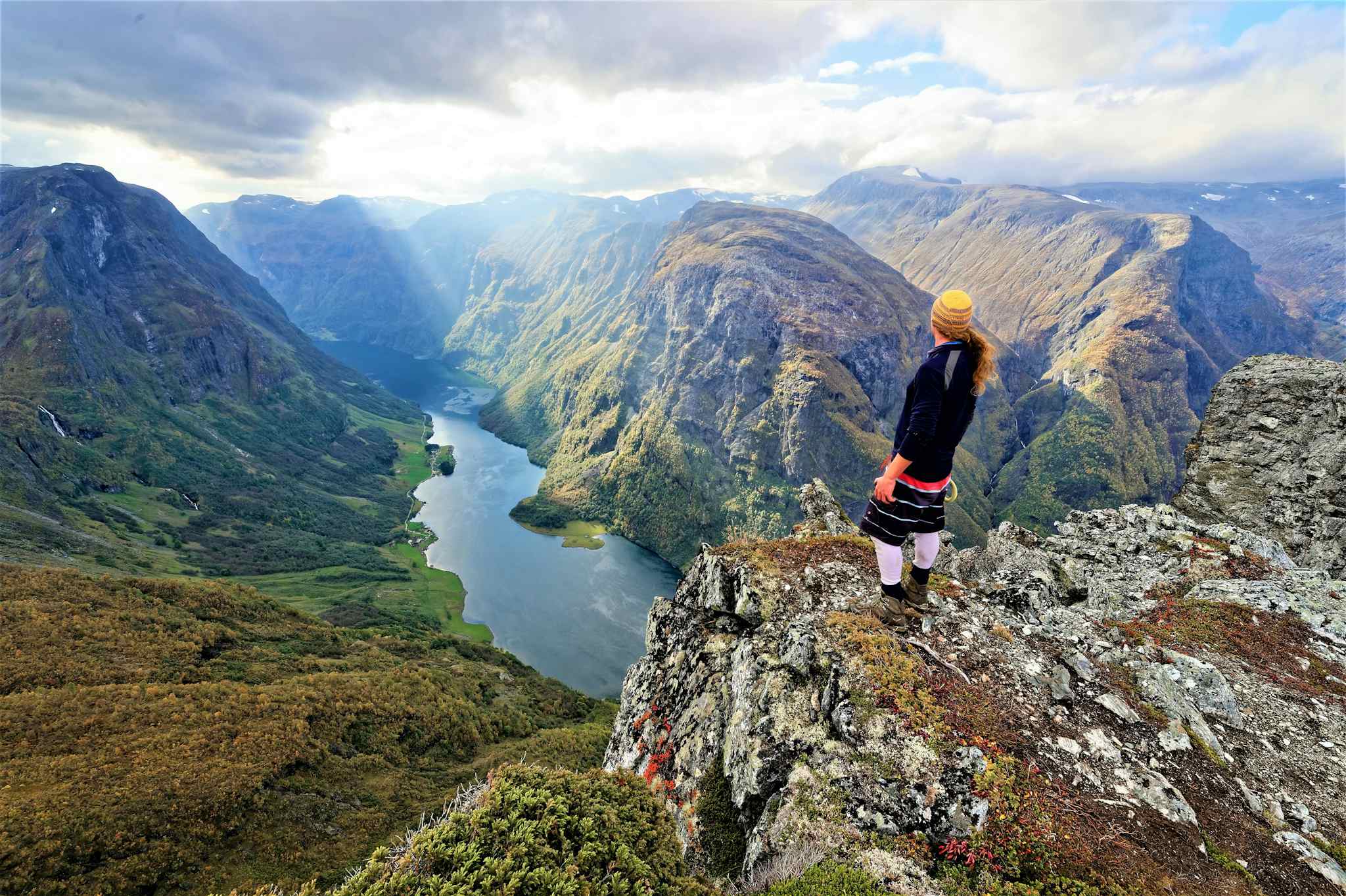 A hiker stands at the edge of the Breiskrednosi summit looking over the Naeroyfjord in the Norwegian Fjords.