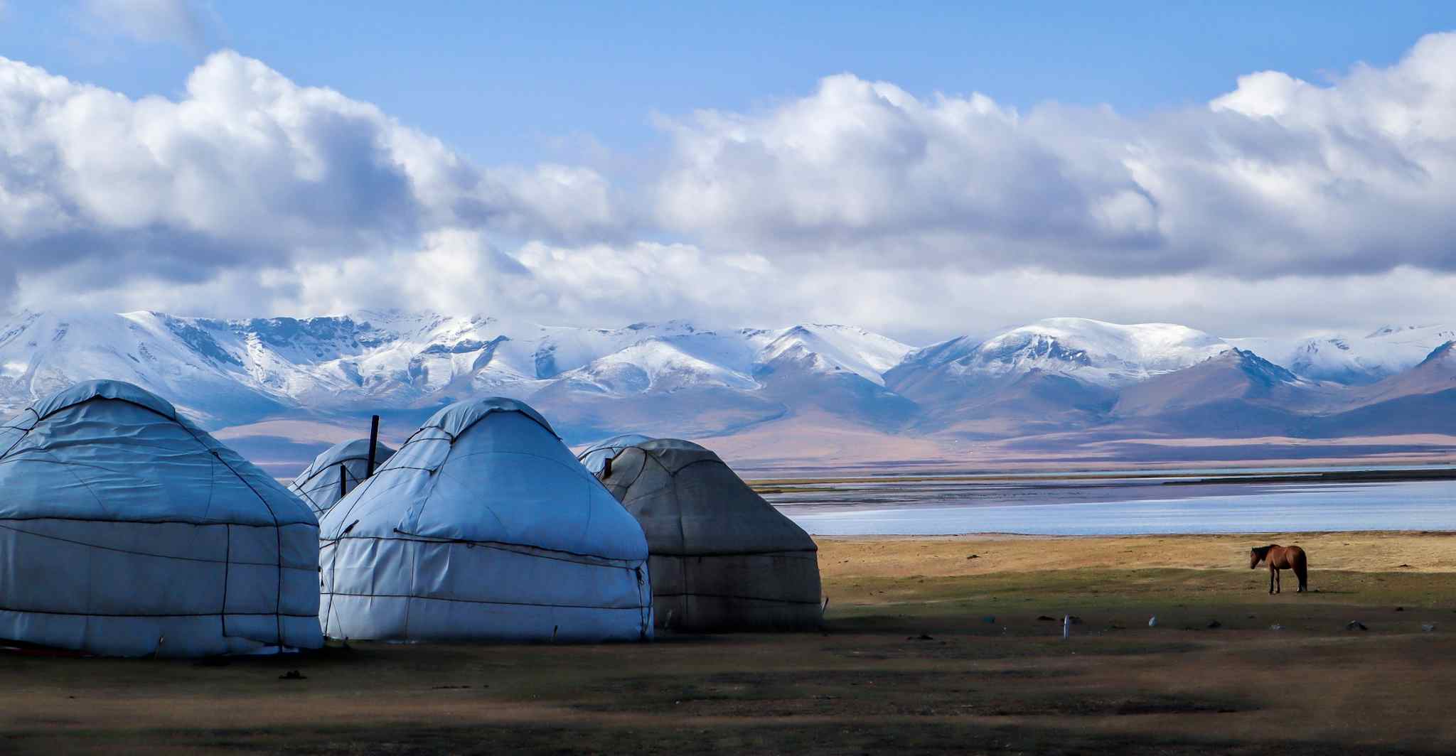 Yurts by Lake Song Kul in Kyrgyzstan, with snow-capped mountains in the background.