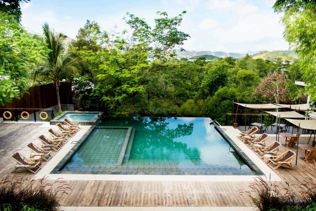 Outdoor pool with lounge chairs looking onto a forest garden