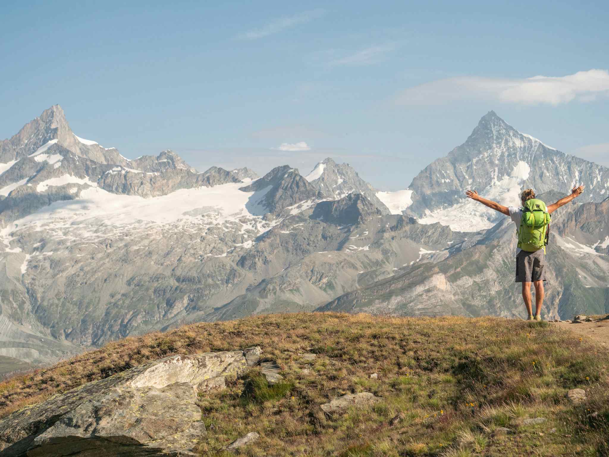 Hiker stands on trail arms outstretched with mountain range behind