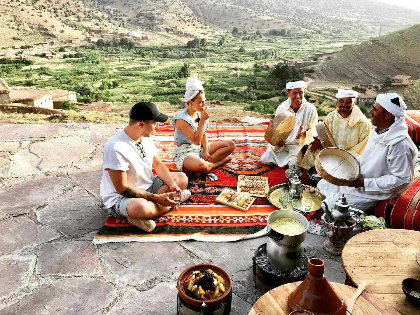 People talking and eating on a Moroccan rug with a view of the valley behind