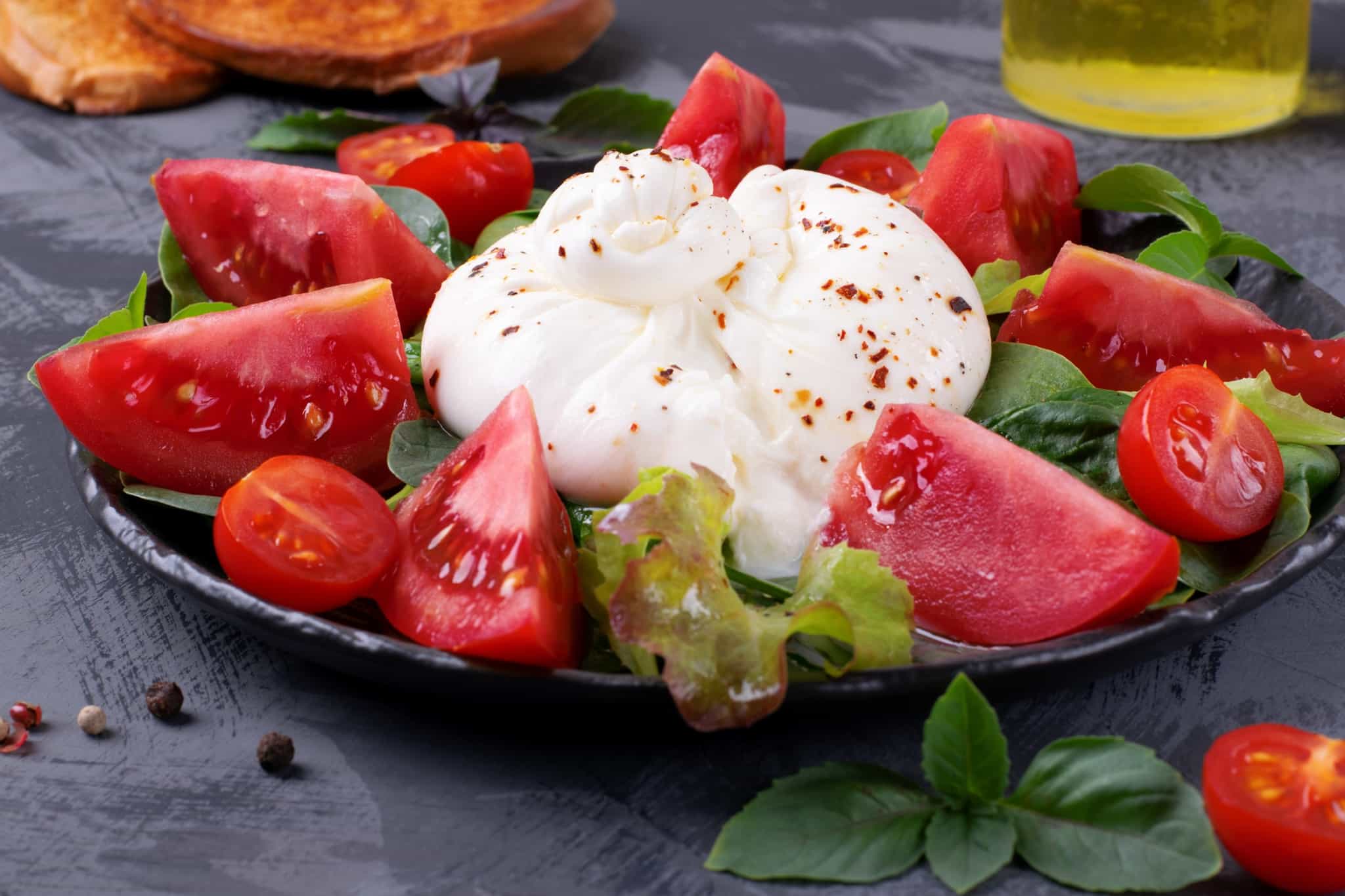 Puglian burrata surrounded by fresh sliced tomato on a plate.