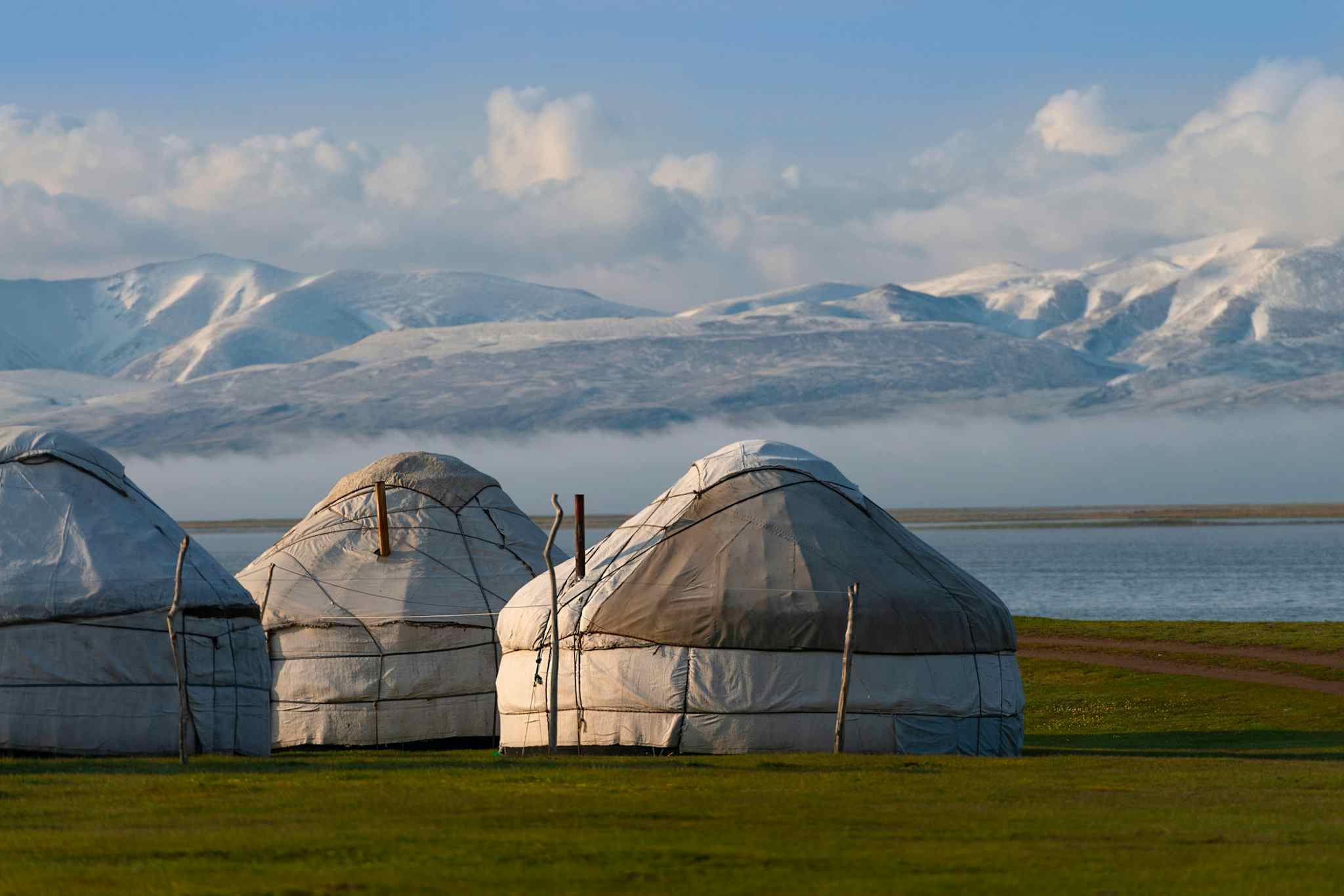 Three yurts by Son Kul lake with mountains in the background in Kyrgyzstan