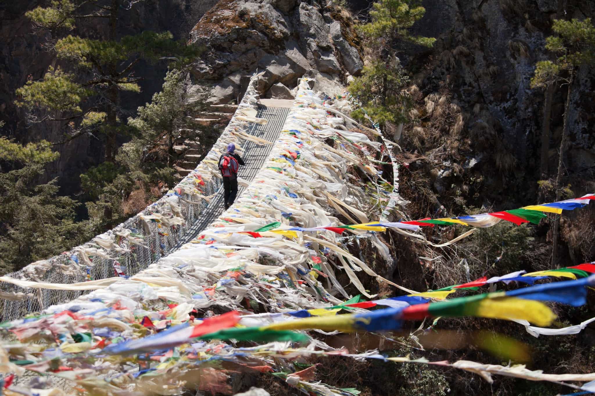 Hiker crossing a suspension bridge in Nepal with prayer flags in the wind