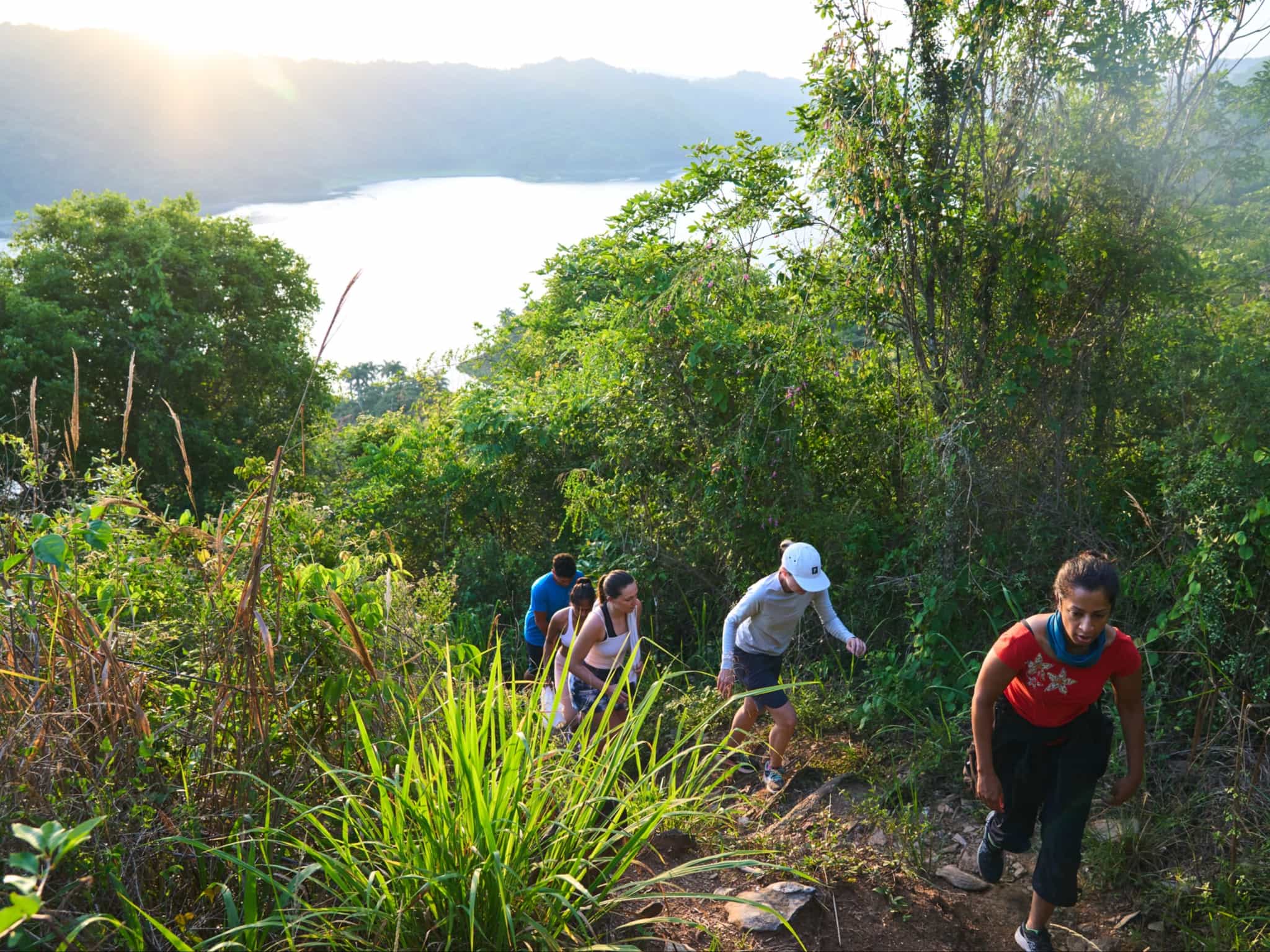 Hikers on a trail through lush vegetation with lake views in Cuba