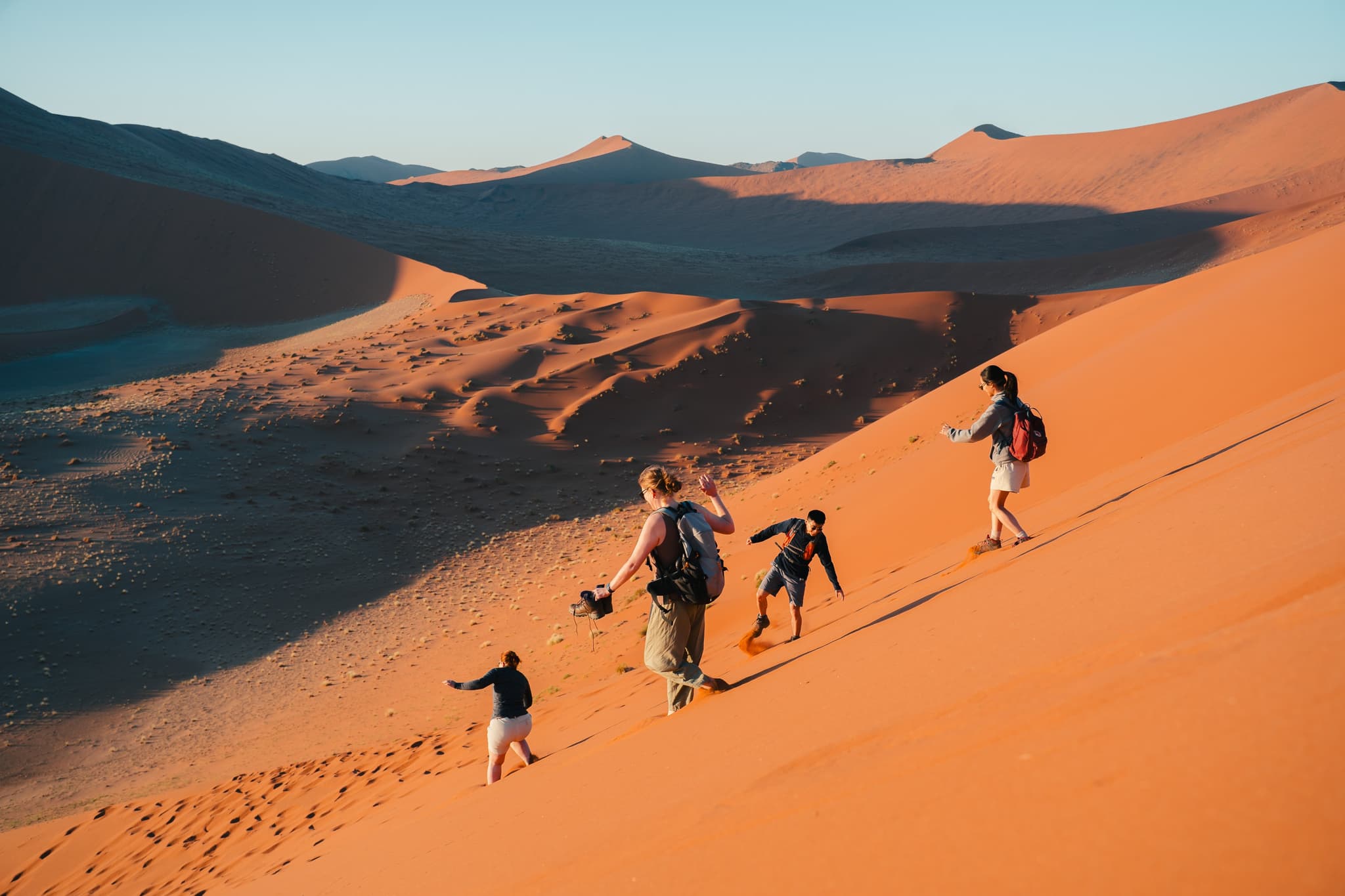 Hikers running down sand dunes in Sossusvlei, Namibia.