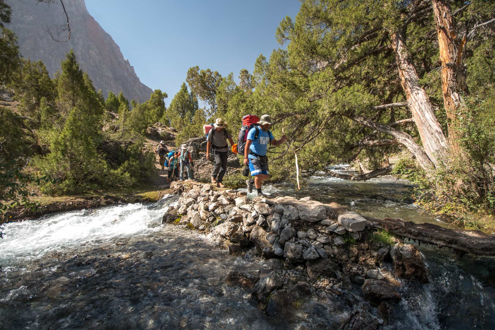 Hikers crossing a shallow river on the way to Alaudin Lakes