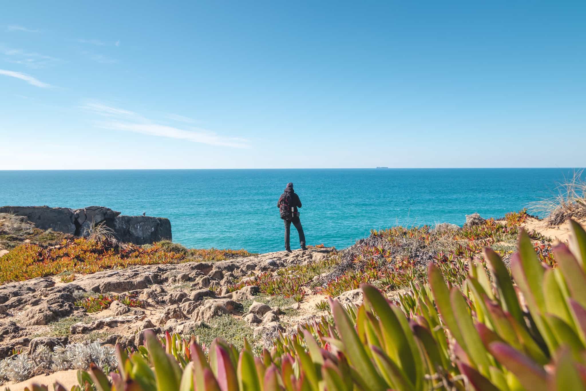 Hiker on rocky cliffs of the Rota Vicentina on the Atlantic Coast near Vila Nova de Milfontes, Odemira, Portugal