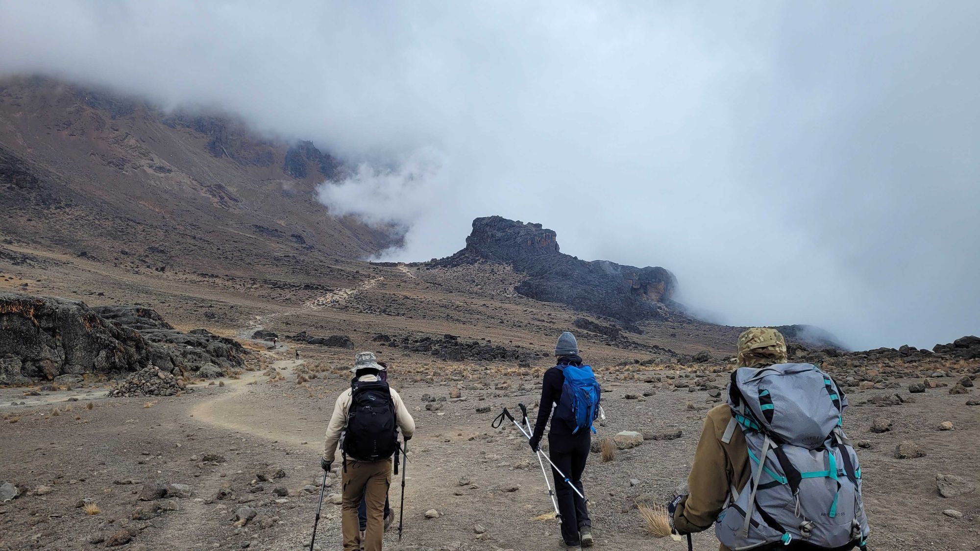 Three hikers following a barren trail to the rock formation Lava Tower on Kilimanjaro, Tanzania.