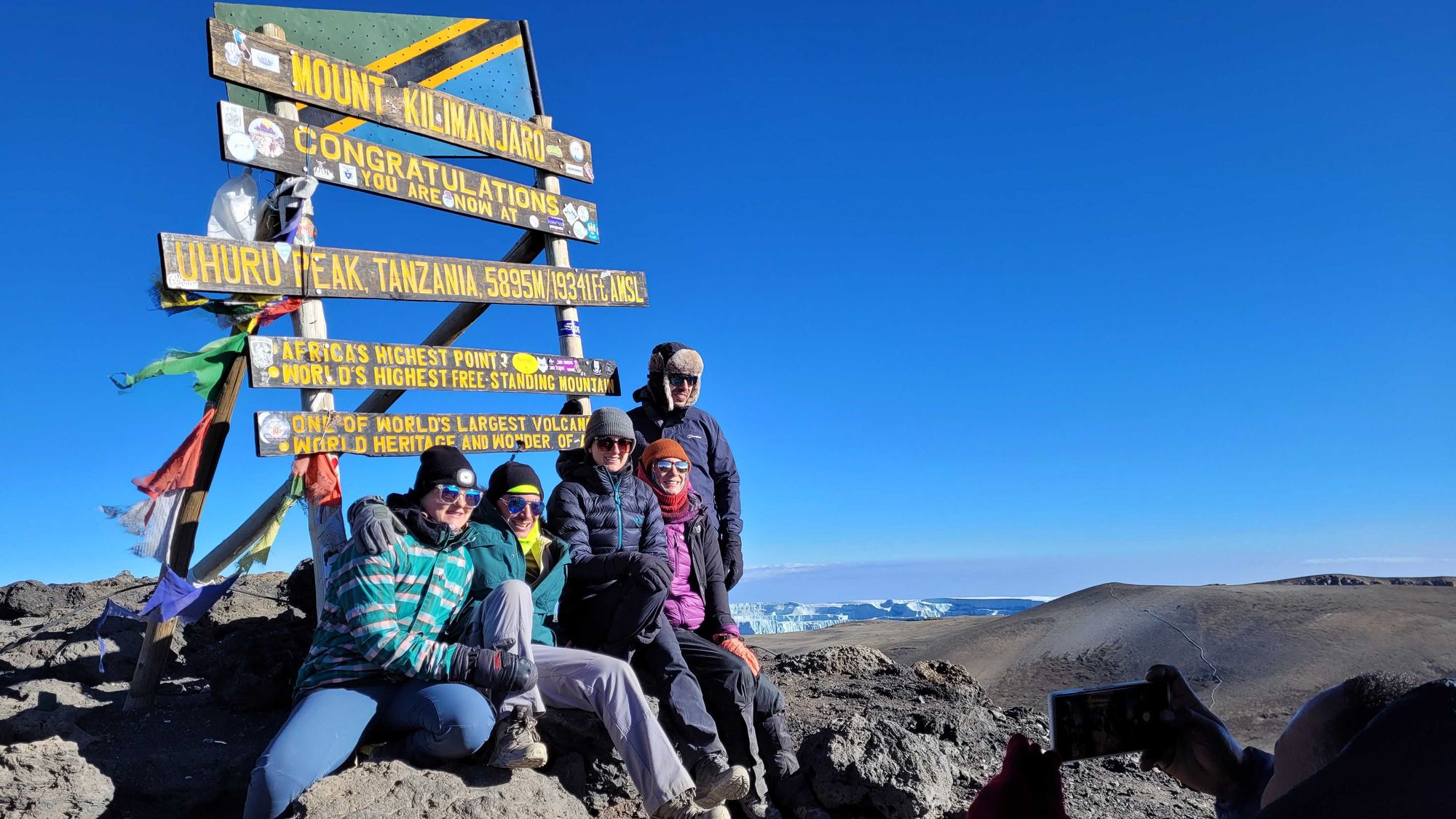 Five trekkers posing for a photo at the Uhuru Peak sign on the summit of Mount Kilimanjaro, Tanzania.