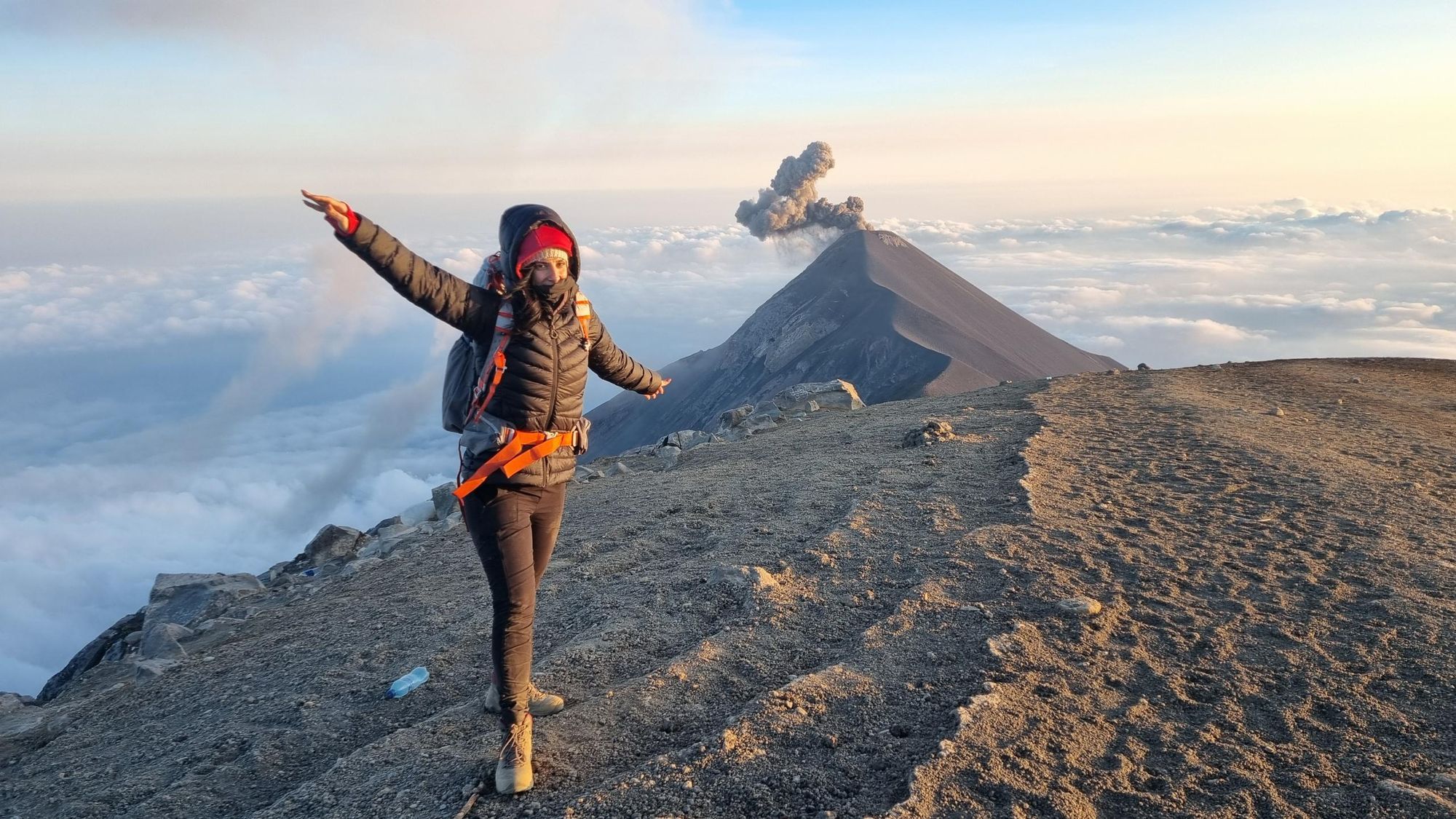 A hiker poses on the summit of Acatenango Volcano, while Fuego erupts in the background