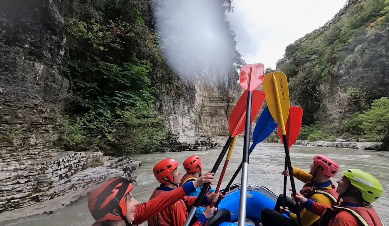 Five rafters with their oars raised in the raft in Albania's Osumi Canyon