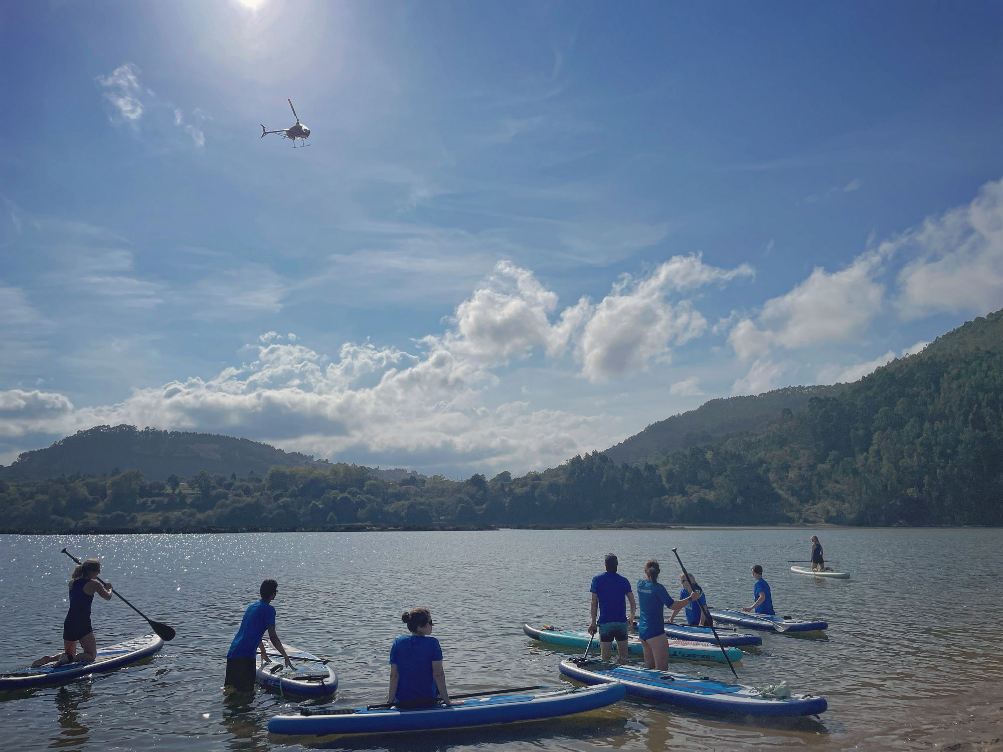 A group of paddleboarders looking out to green hills across an estuary on the Asturian coast in Spain.