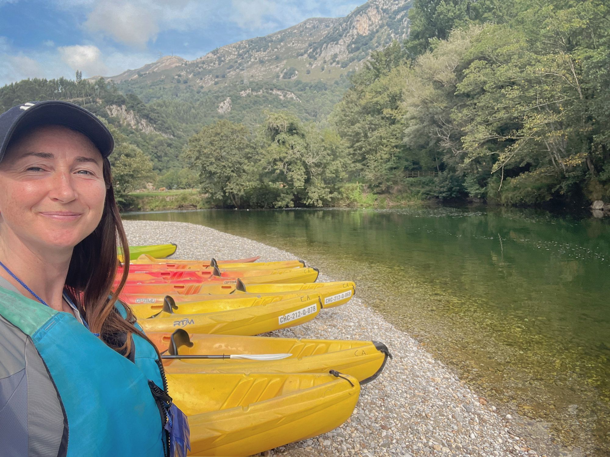 A woman and yellow kayaks on the bank beside the Rio Deva in Spain.