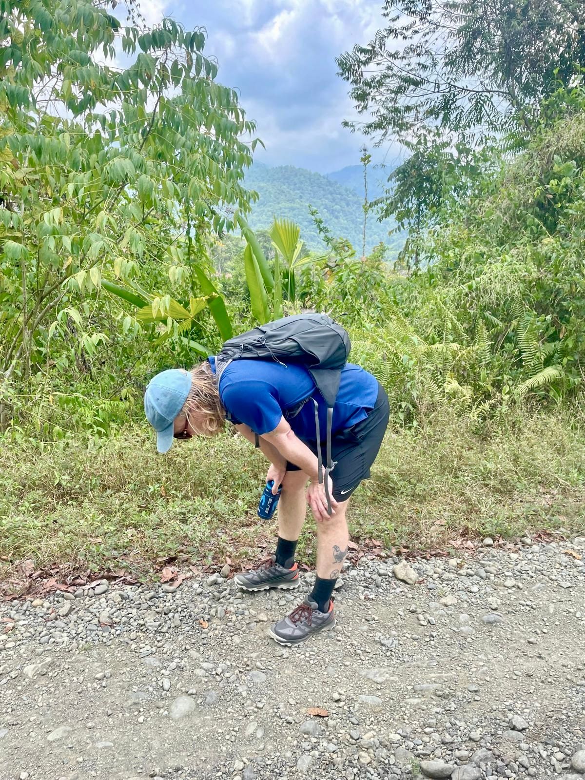 A man bent over on a dirt track backed by forest.