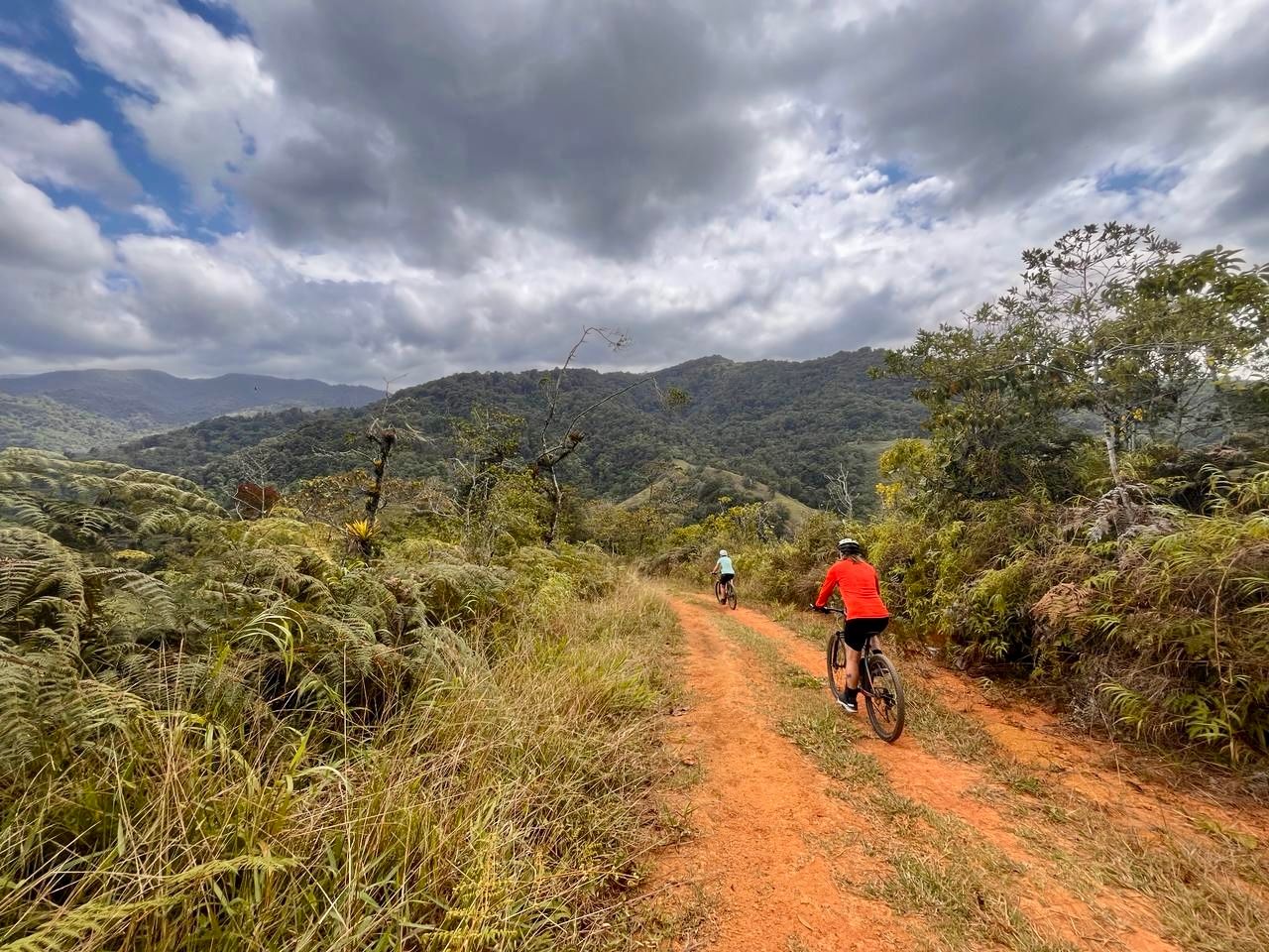 Two cyclists on a dirt track in Costa Rica among forested landscapes.