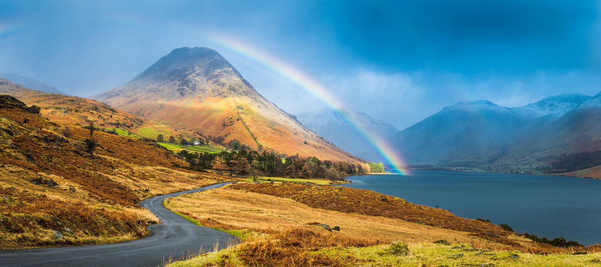 A road winding along the blue shore of Wast Water and Yewbarrow, overlooked by the snowy peaks of Great Gable and Scafell. Photo: Getty