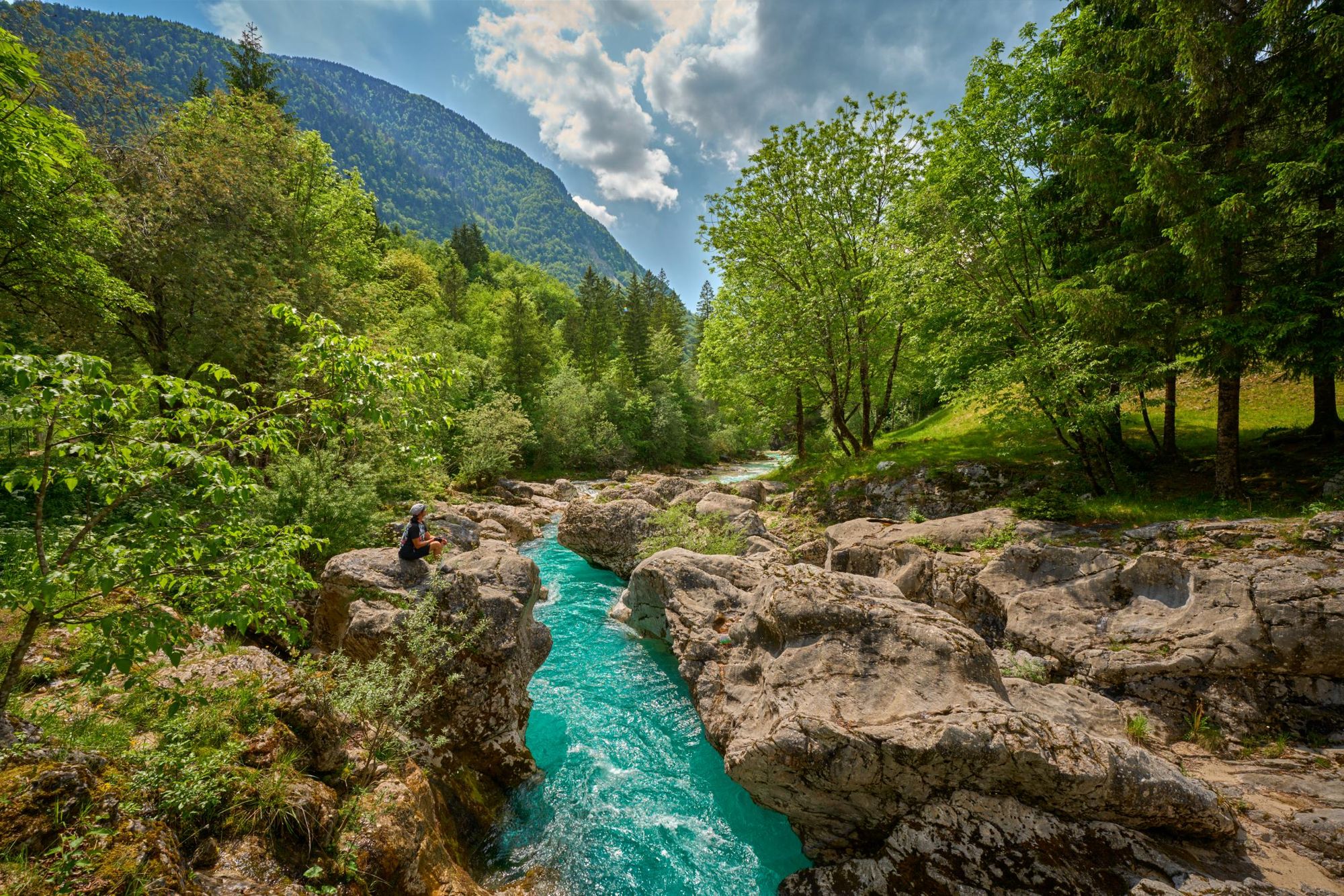 The inimitable colour of the Soča River, rlined by rocks and greenery, with mountains behind. Photo: Getty