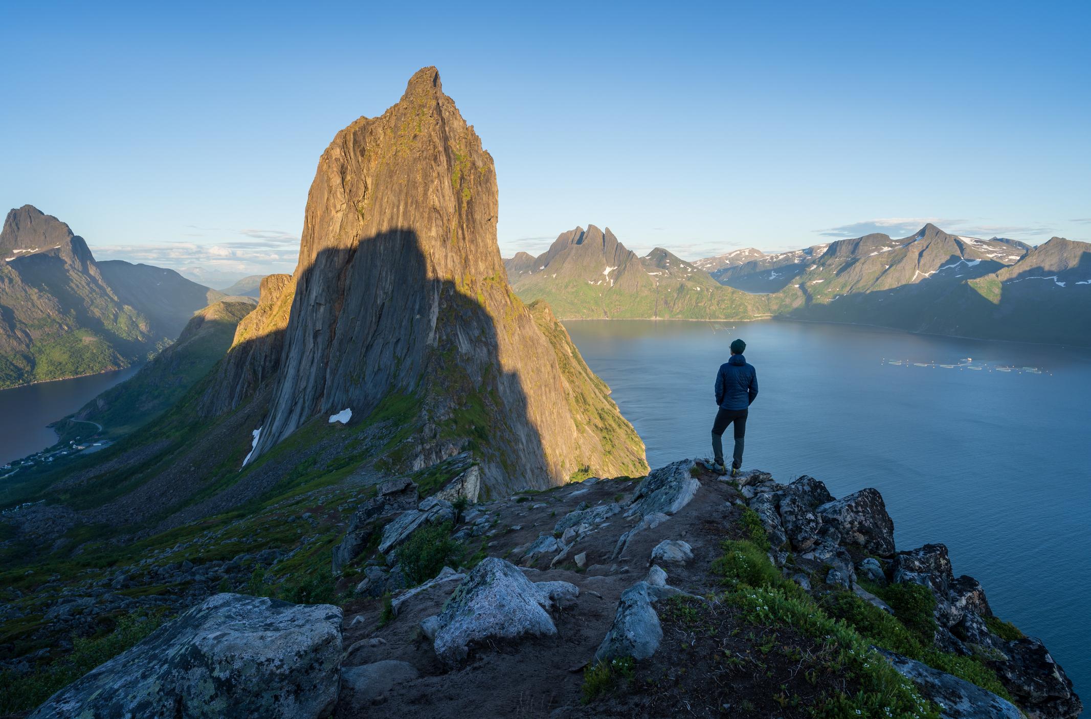 A man looks at the jagged peak of Segla, a mountain in Norway.