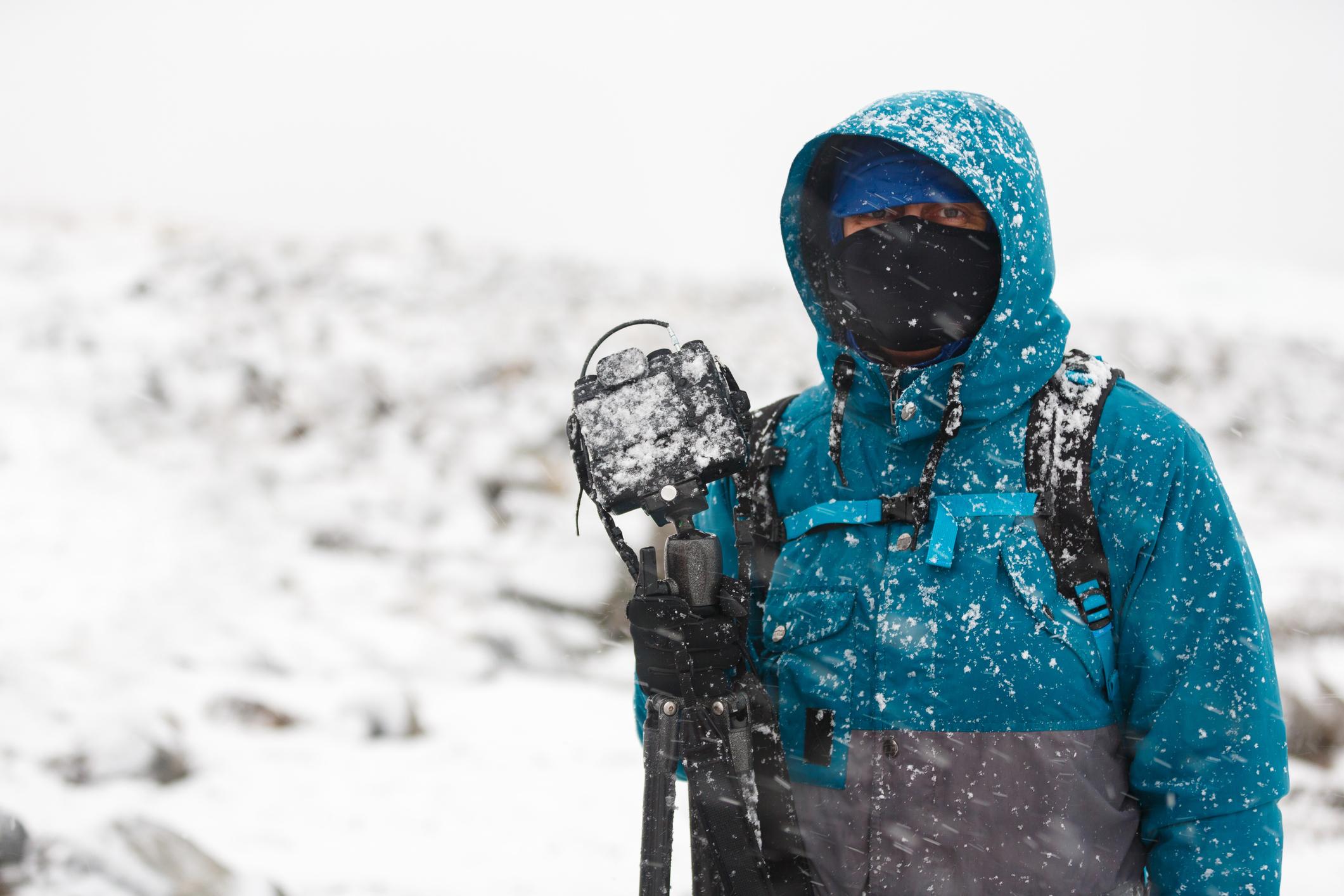 A man stands in a snowstorm, holding a camera. Photo: Getty