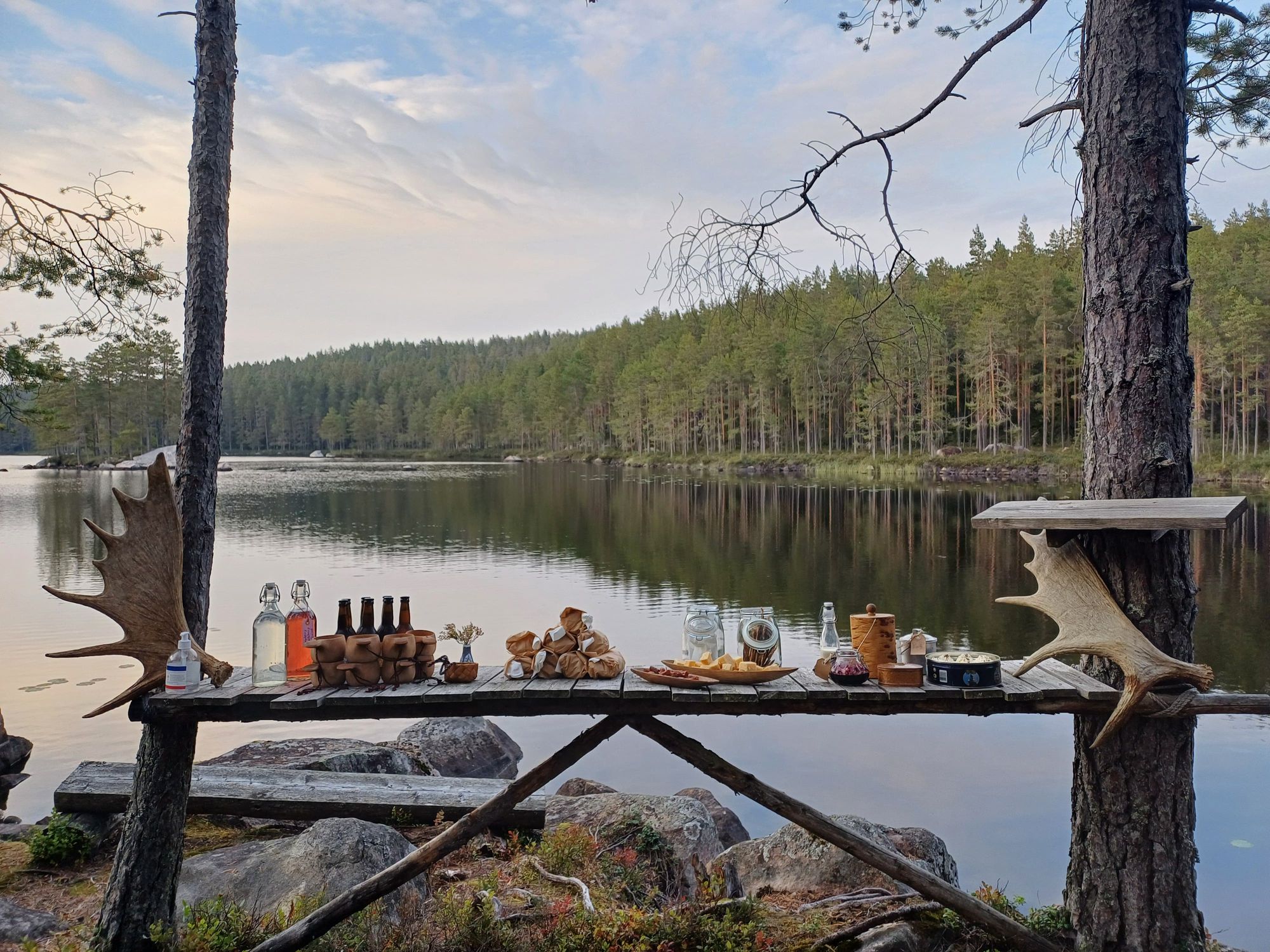 Food and drinks set up on a wooden board in front of a tranquil lake view.