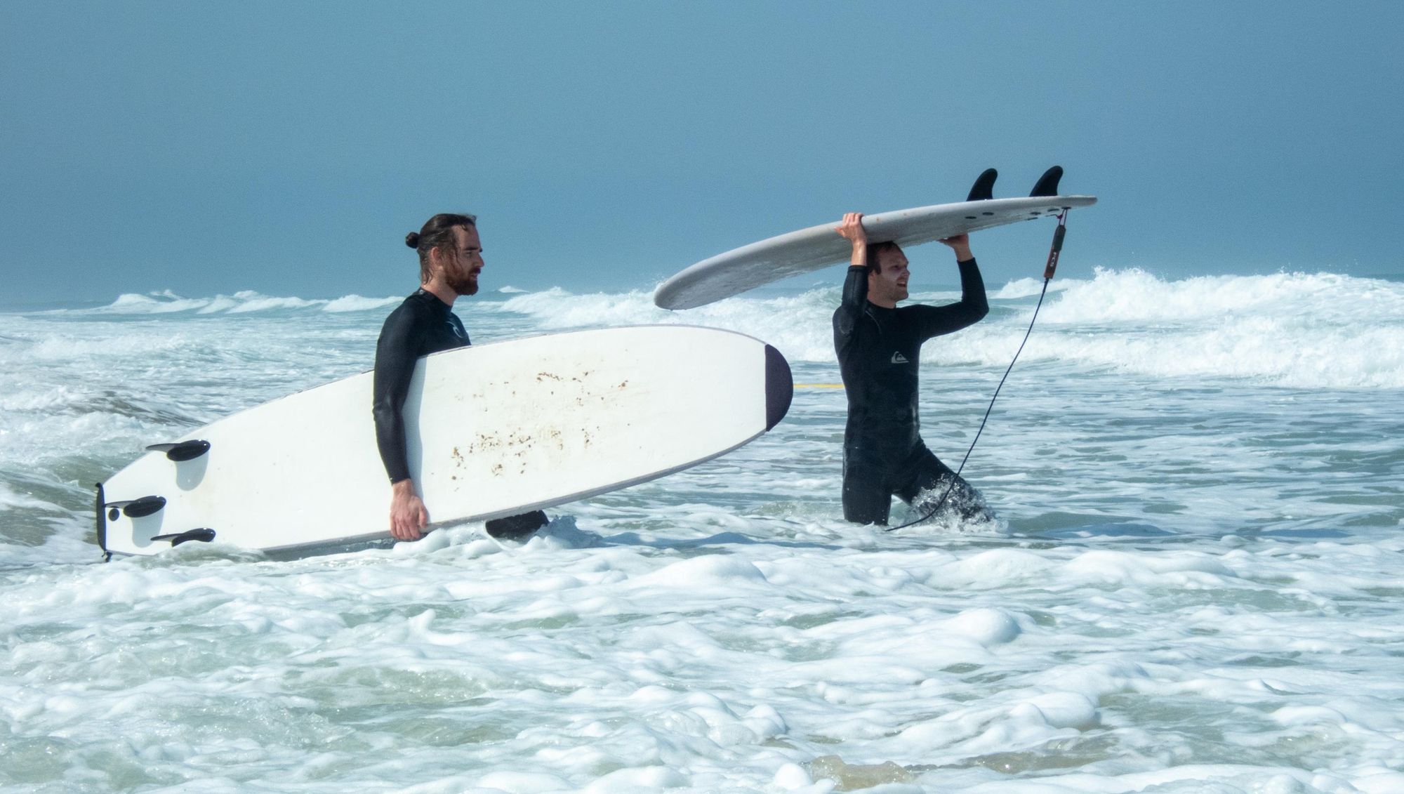 Two surfers carry their boards into the waves.